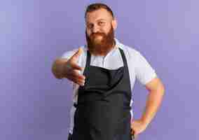 Free photo professional bearded barber man in apron with confident expression offering hand greeting standing over purple wall