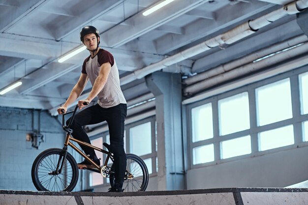 Профессиональный гонщик BMX в защитном шлеме готовится к прыжку в скейтпарке в помещении