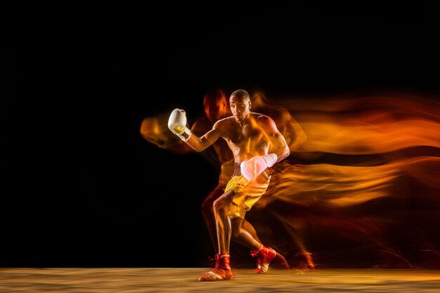 Professional boxer training isolated on black studio background in mixed light