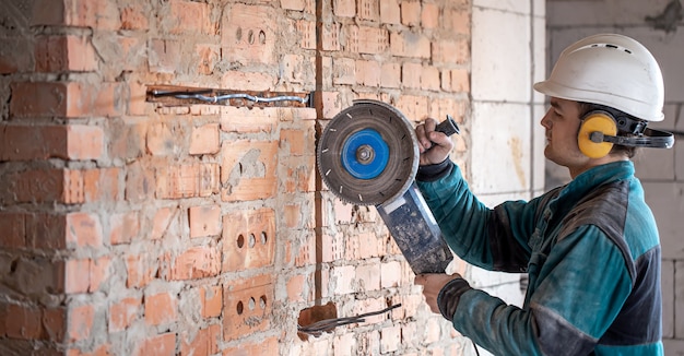 A professional builder in work clothes works with a cutting tool.
