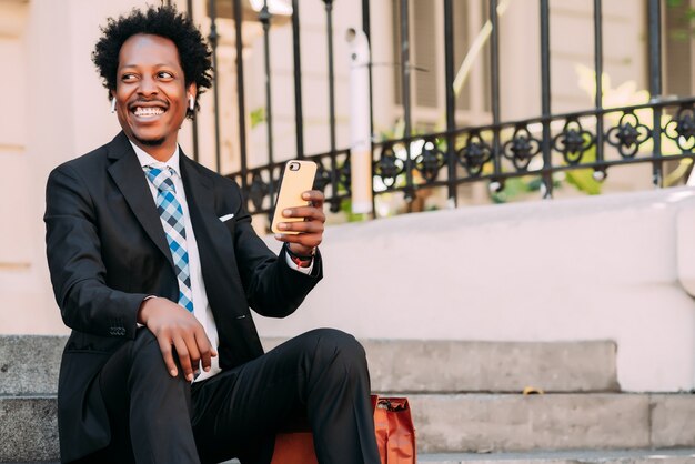 Free photo professional businessman using his mobile phone while sitting on stairs outdoors