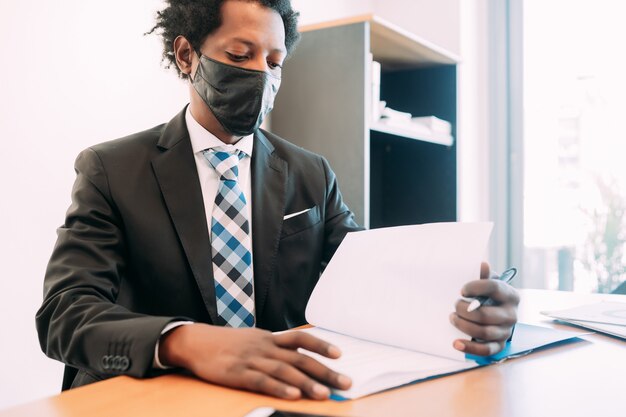 Профессиональный бизнесмен в маске для лица во время работы с некоторыми файлами и документами в своем офисе.
