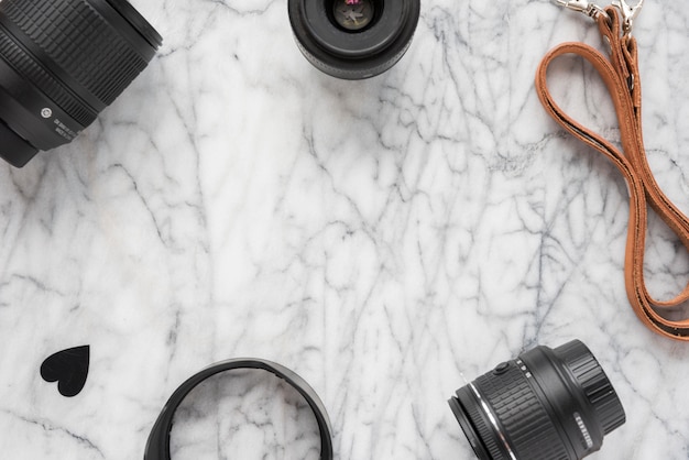 Foto gratuita obiettivo della fotocamera professionale; anelli di prolunga con cuori e cintura sul pavimento di marmo