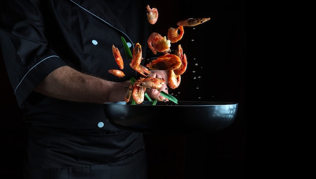 Professional chef cooks shrimp in a pan with vegetables freezing in motion free advertising space