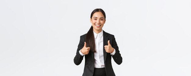 Профессиональная уверенная в себе улыбающаяся азиатская деловая женщина уверяет, что все идет отлично, показывает большой палец вверх, рекомендует агентство или продукт, например, и одобряет, говорит: «Молодец, хорошая работа» или «Хорошая работа».