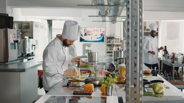 Professional cook using grater to make shredded cheese for italian food recipe in restaurant kitchen. Male chef in uniform grating parmesan ingredient to prepare delicious culinary gourmet meal.