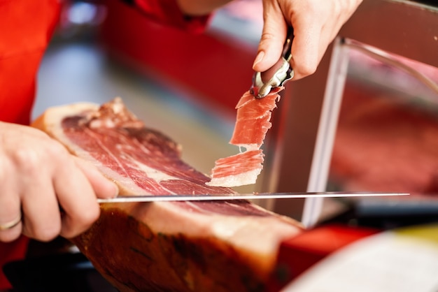 Professional cutter carving slices from a whole bone-in serrano ham