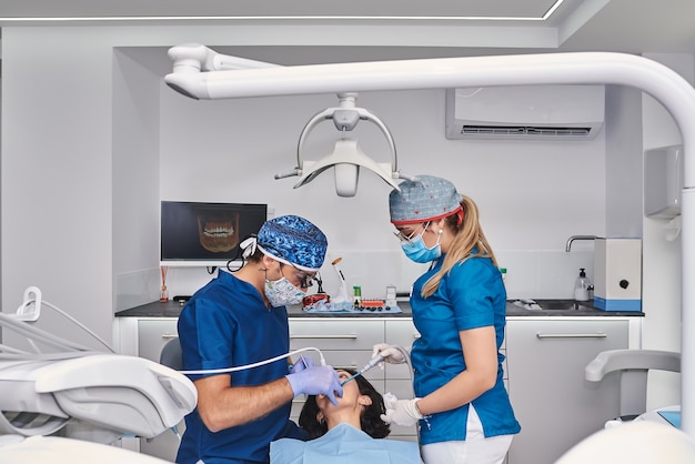 Профессиональные стоматологи исследуют зубы женщины в стоматологическом кабинете.