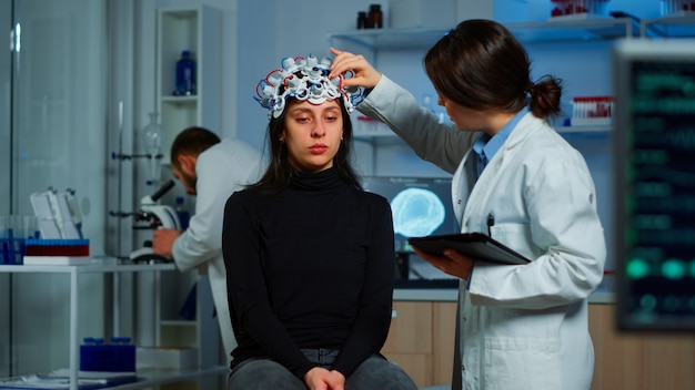 Professional doctor in neuroscience developing treatment for neurological diseases examining patient evolutions. Doctor researcher adjusting EEG headset analyzing brain functions and health status