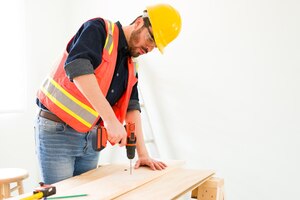 Professional engineer and contractor drilling a wooden panel. male carpenter with a safety helmet working on building some furniture