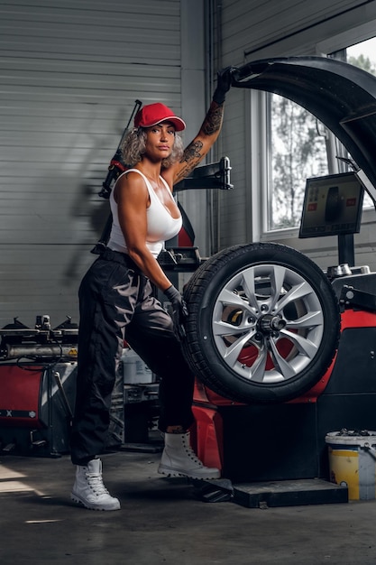 Professional female auto mechanic is fixing broken car at auto workshop near window.