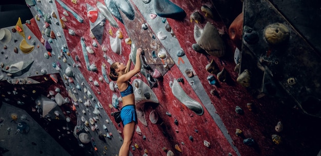 Professional female climber on a bouldering wall indoors.