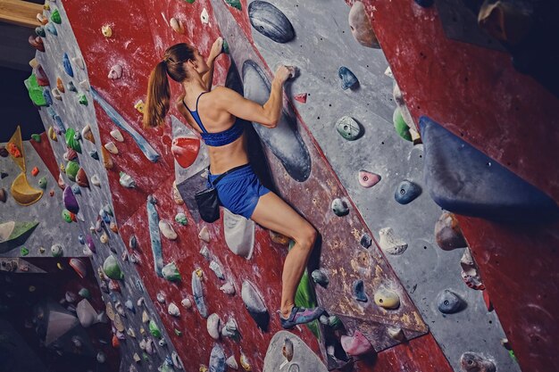 Professional female climber on a bouldering wall indoors.