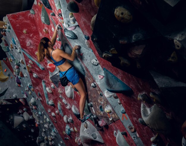 Professional female climber on a bouldering wall indoors.