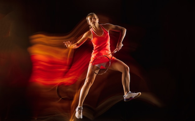 Professional female tennis player training isolated on black studio background in mixed light. Woman in sportsuit practicing.