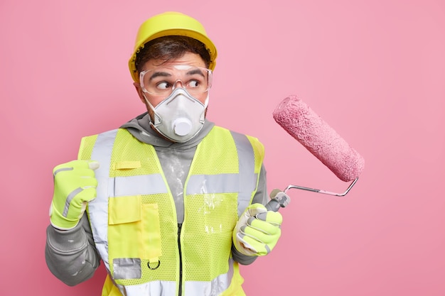 Free photo professional foreman or construction worker in protective helmet face mask and uniform holds paint roller clenches fist