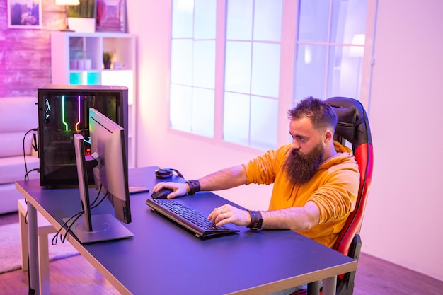 Профессиональный геймер с длинной бородой перед мощным игровым оборудованием в комнате, залитой неоновыми огнями