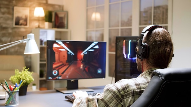 Free photo professional gamer with long hair puts his headphones with a mic on and starts playing shooter game on personal computer.