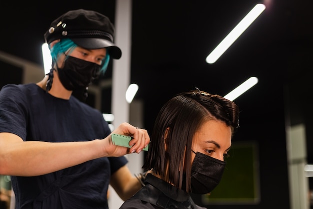 A professional girl hairdresser makes a client haircut. The girl is sitting in a mask in beauty the salon