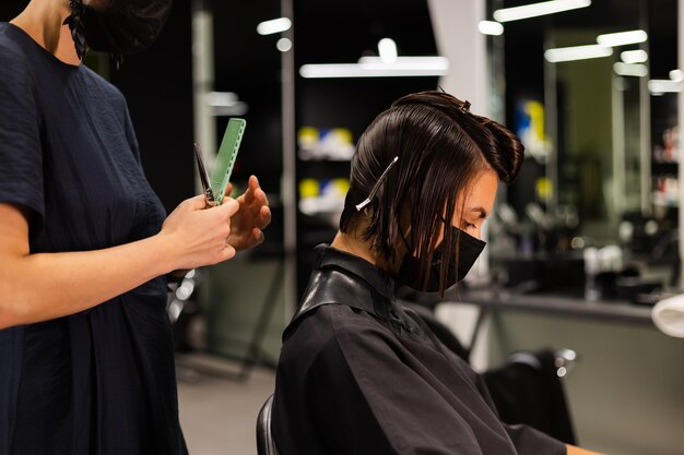 A professional girl hairdresser makes a client haircut. The girl is sitting in a mask in beauty the salon