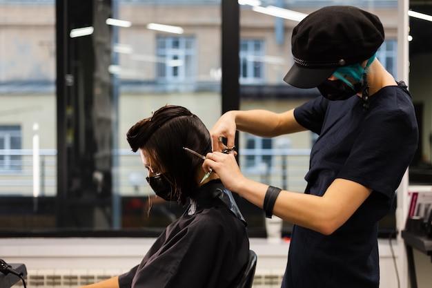 Un parrucchiere ragazza professionista fa un taglio di capelli del cliente. la ragazza è seduta in una maschera nel salone di bellezza