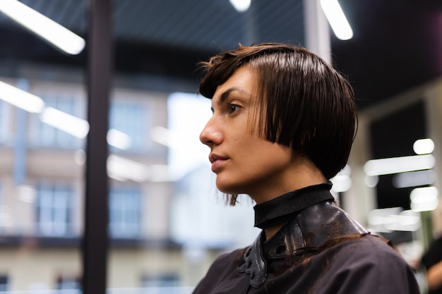 A professional girl hairdresser makes a client haircut. The girl is sitting in a mask in beauty the salon