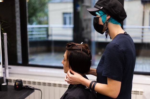 Профессиональный парикмахер делает клиентскую стрижку. Девушка сидит в маске в салоне красоты