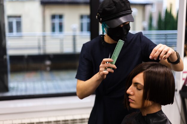 A professional girl hairdresser makes a client haircut. The girl is sitting in a mask in beauty the salon