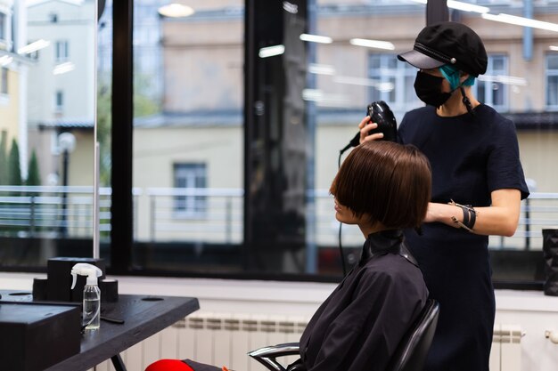 A professional girl hairdresser makes a client haircut. The girl is sitting in a mask in beauty the salon