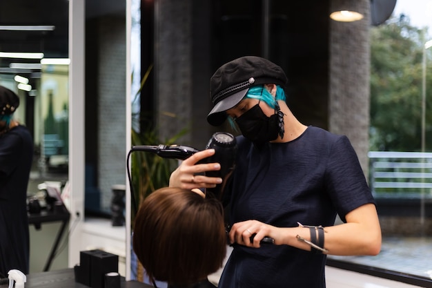 Un parrucchiere ragazza professionista fa un taglio di capelli del cliente. la ragazza è seduta in una maschera nel salone di bellezza