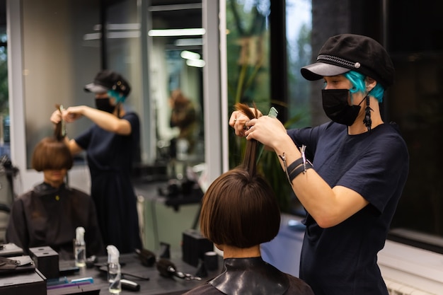 A professional girl hairdresser makes a client haircut. The girl is sitting in a mask in beauty the salon