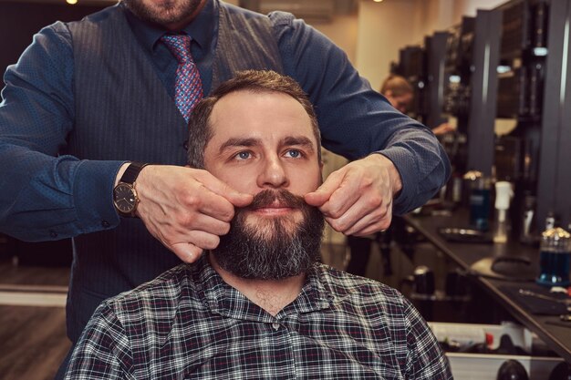 Professional hairdresser modeling beard at the barbershop. Close-up photo.