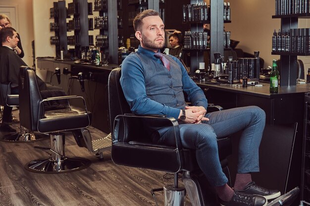 理髪店の椅子に座って次の顧客を待っているプロの美容師。