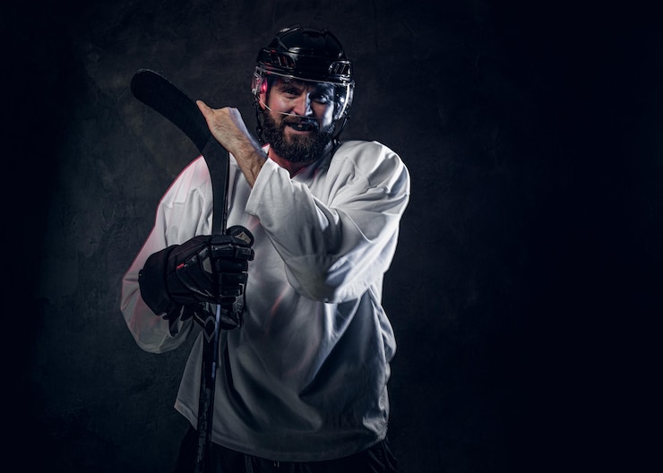 Free Photo professional hockey player in helmet is posing with hockey stick at photo studio.