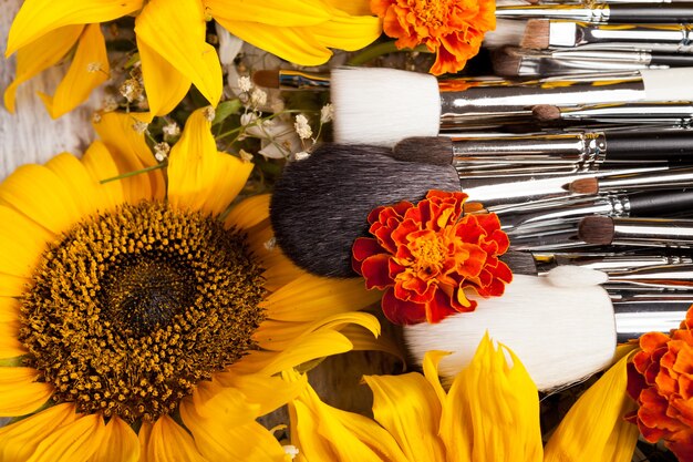 Professional Make up brushes next to beautiful wild flowers on wooden background