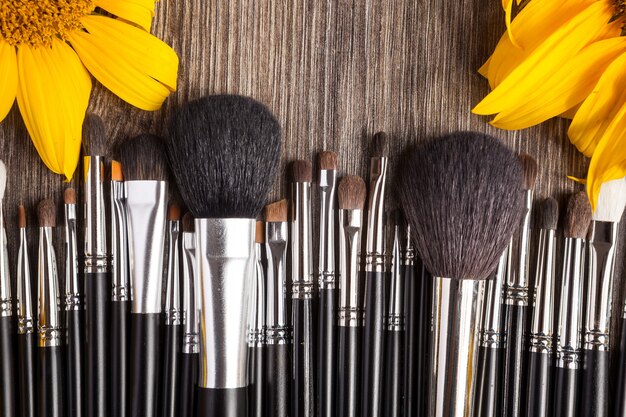 Professional Make up brushes next to beautiful wild flowers on wooden background