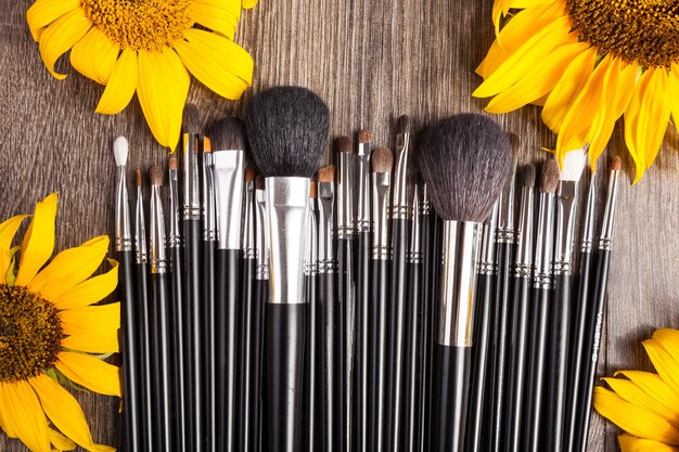 Professional Make up brushes next to beautiful wild flowers on wooden background