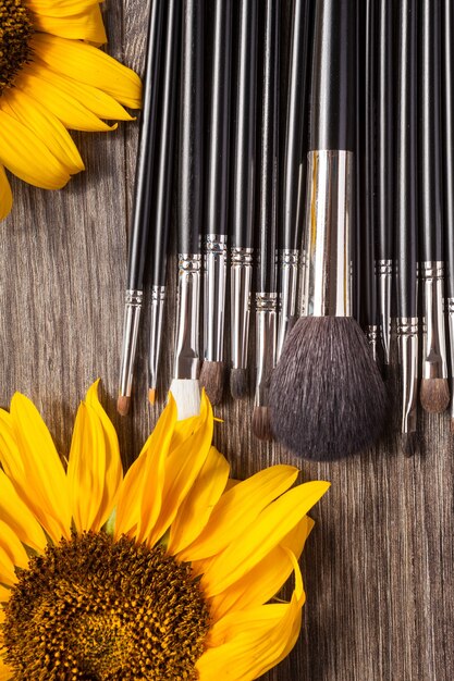 Professional Make up brushes next to beautiful wild flowers on wooden background