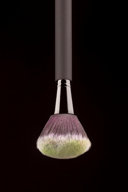 Professional makeup brush with yellow powder on black background