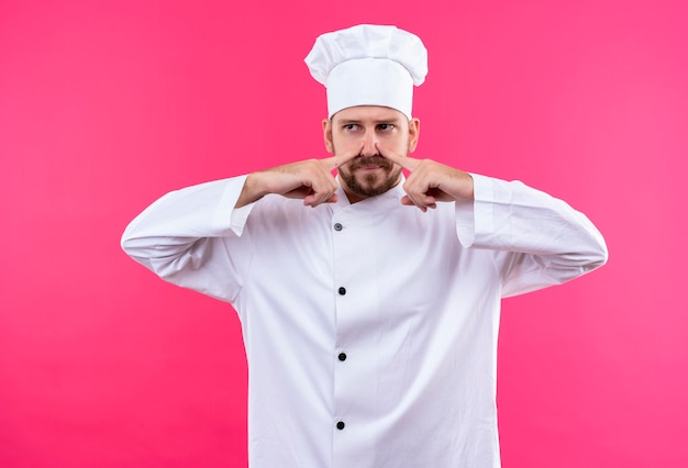 Professional male chef cook in white uniform and cook hat closing nose, bad smell concept over pink background