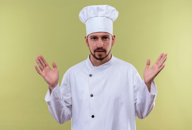 전문 남성 요리사 흰색 유니폼 요리와 녹색 배경 위에 자신감 서 찾고 손을 올리는 요리사 모자
