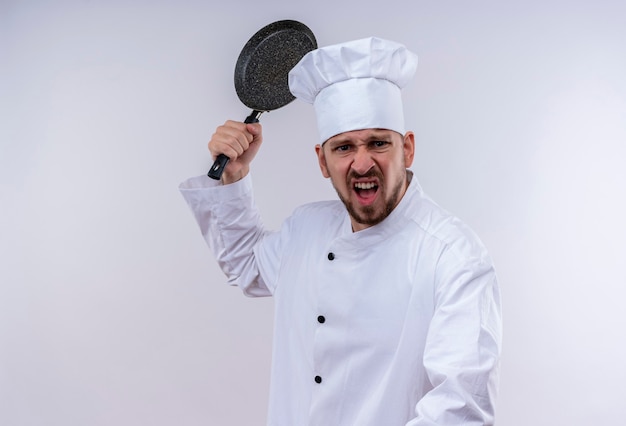 Free photo professional male chef cook in white uniform and cook hat swinging a frying pan with aggressive expression standing over white background