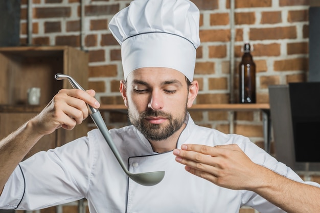 レードルでおいしいスープを嗅ぐプロフェッショナルな男性シェフ