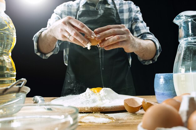 Professional male cook sprinkles dough with flour