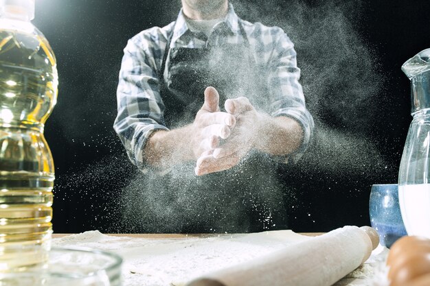 Professional male cook sprinkles dough with flour