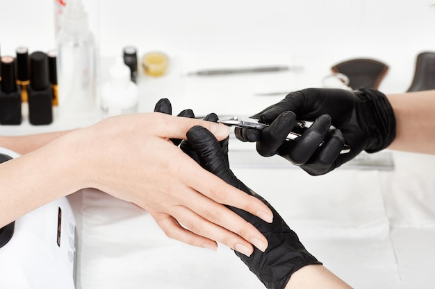 Professional manicurist in black gloves provides service to client making manicure with manicure cuticle trimmer.