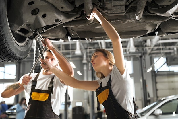 Professional mechanics standing under automobile and working