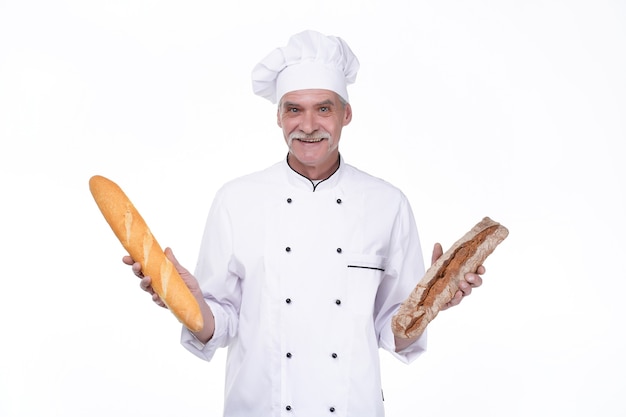 Vecchio fornaio professionista in uniforme che tiene baguette con pane rimanendo sul muro bianco