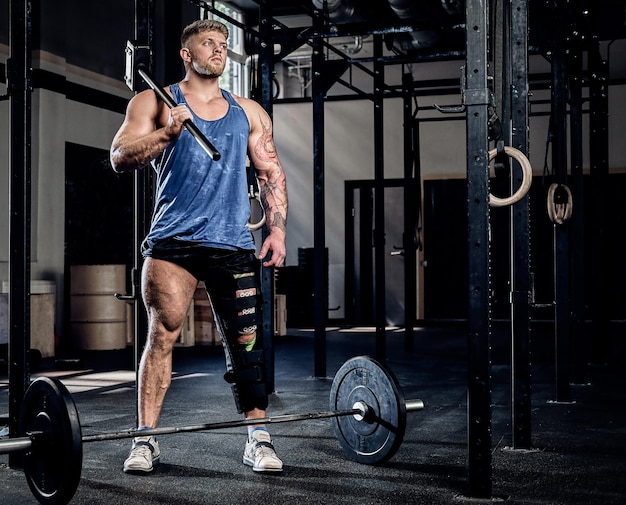 Professional powerlifter with a bandage on a leg, holding a sports hammer, warming up before training, injury recovery. Sport, commitment, motivation