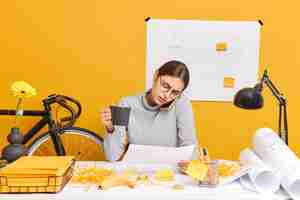 Free photo professional skilled female architect has telephone conversation with colleague concentrated into papers prepares engineering project drinks coffee poses in coworking space. busy woman engineer